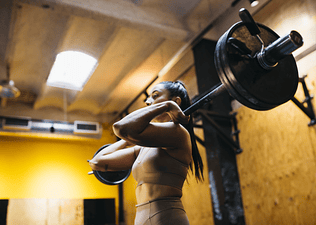 Woman lifting a loaded barbell in a gym doing a strength training program for increasing training volume.