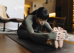 Woman doing a Seated Forward Fold in her living room at home during a practice of seated yoga poses