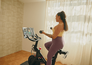 Woman working out on a Peloton Bike doing a light-weight, high-rep arm workout.
