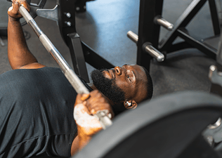 Man at the gym doing a bench press with a weighted barbell.