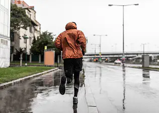 Man running in the rain through a city in an orange rain jacket