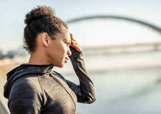 A woman standing outside and holding her hand to her face as she suffers from a headache after a workout.