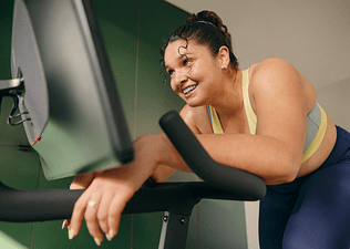 Woman on a Peloton Bike resting after doing a workout finisher.