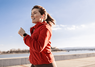 A happy woman going a run outside. She's wearing a red zip-up hoodie.