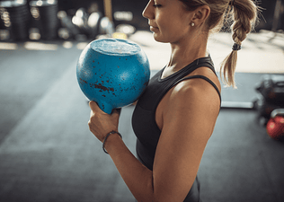 Woman doing the kettlebell halos exercise in a gym with a blue kettlebell.