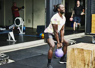 Man in a gym doing kettlebell squats with a 20lb purple kettlebell
