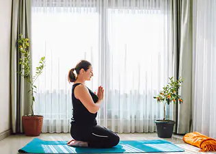 A woman in Hero Pose with prayer hands. She is practicing yoga at home to improve her mindset.