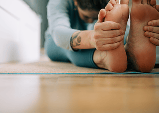 Woman with tattoos doing a Seated Forward Fold while doing yoga for flexibility at home.