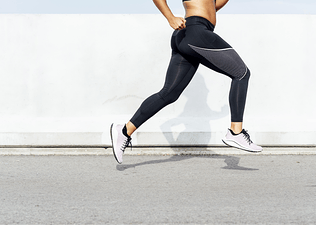 Close up shot of a woman's legs while she's running strides outside.