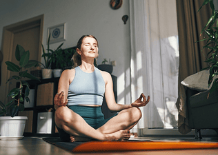 A woman meditating at home in the sunlight as part of her morning routine.