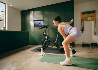 Woman engaging in hybrid training by doing a Peloton kettlebell strength class on her Bike+.