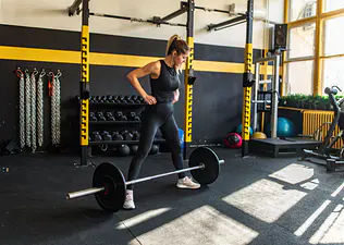 Woman in a gym preparing to do a sumo deadlift with a loaded barbell.