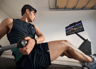 Man working out in his garage gym with the Peloton Cross Training Row+ using the strength exercise form feedback feature.