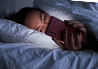 A woman practicing revenge bedtime procrastination by scrolling on her phone in bed late at night.