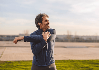 A happy, mature man stretching his arms before exercising outside.
