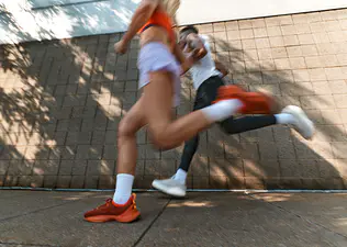 Two runners in motion blur sprint past a brick wall outdoors.