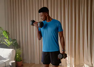 Man doing dumbbell biceps curls during a home strength workout.