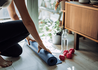 Woman rolling out exercise mat for a home workout deciding whether to do Pilates vs weight training