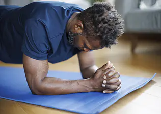 Man in a blue shirt doing a forearm plank during a bodyweight workout at home
