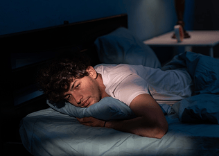 A man lying awake in his bed. He can't sleep after exercising.