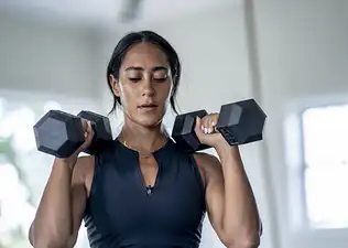 A woman working out efficiently. She is preparing to do a compound exercise with her dumbbells and an overhead press movement. 