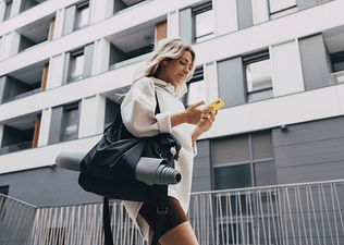 Woman carries gym bag with yoga mat while using a mobile phone