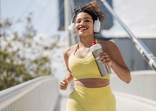 Woman running outside with headphones on holding a water bottle