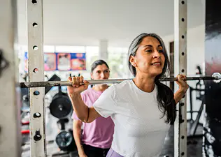 Woman squatting a barbell to build strength while exercising during menopause.