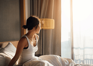 A woman waking up early. She's sitting up in bed and looking out the window.