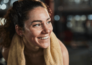 A happy, sweaty athlete smiling and looking to the side. There's a towel around her neck.