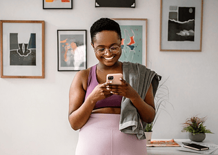 Woman smiling and looking at her phone, texting her virtual workout buddy after exercising.
