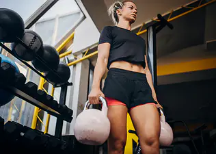 Young woman in the gym holding two kettlebells while doing a farmer's carry exercise