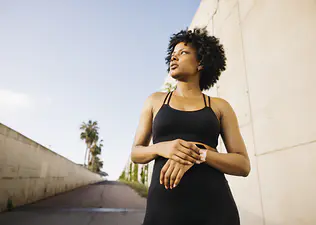 A young woman outside in workout clothes checking her smartwatch deciding whether to run faster or longer