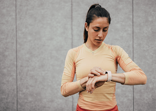 Young woman in fitness gear checking her heart rate zone on a smartwatch during her long run