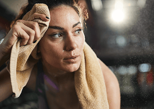 A sweaty athlete feeling lightheaded after a workout. She's resting and has a towel behind her neck and on her forehead.
