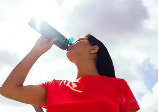 An athlete in a red shirt drinking from a water bottle on a sunny day.