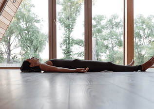 Side view of woman on the ground in Savasana (corpse pose)