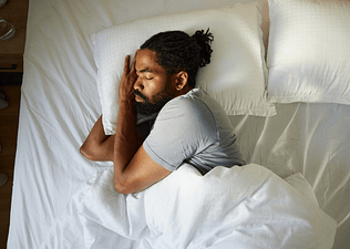 A man sleeping soundly in bed, lying on his side.