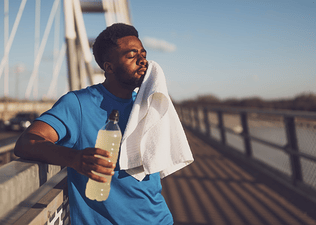 A man experiencing tooth pain after running. He is holding a white towel up to his jaw and closing his eyes while resting and holding a sports drink.