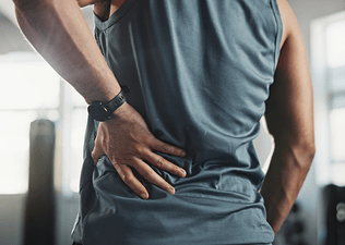 A close-up photo of a man holding his lower back. He's experiencing lower back pain after cycling.