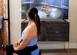 Woman stretches while watching Peloton instructor on TV
