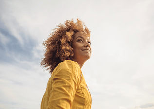 A low-angle portrait of a woman looking up at the sunny sky.