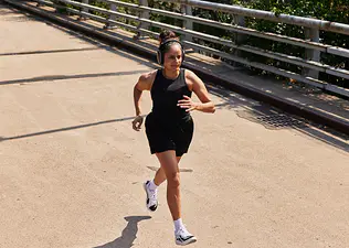 A woman running on an outdoor bridge on a sunny day.