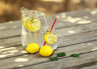 A pitcher and a glass of lemon water on a wooden picnic table
