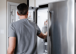 A back view of a man reaching into his fridge for food after a workout.