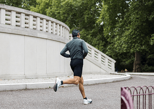 A photo of a man from the back as he goes on a run outdoors. He's wearing biker shorts, a long sleeve shirt, and sunglasses.
