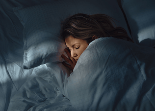 A woman spending time in deep sleep. She's asleep under the covers in a dark bedroom.
