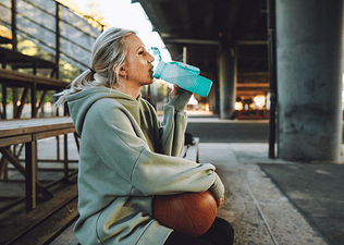 A woman drinking an electrolyte drink after an outdoor basketball game.