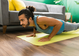 A man in Plank Pose on a yellow yoga mat at home. He is doing yoga to build muscle.