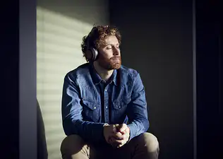 A man practicing healing meditation. He's listening to a meditation on his headphones, closing his eyes, and sitting down.